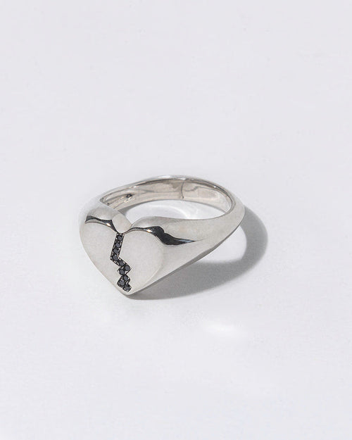 Silver ring with black diamonds in a broken heart shaped signet on a white background