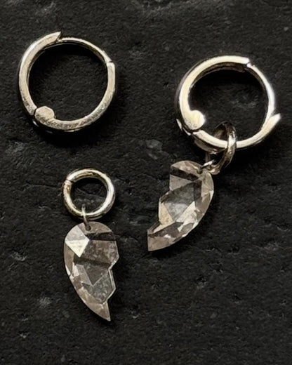 Pair of silver hoops with broken heart diamonds dangling as a charm on a black background