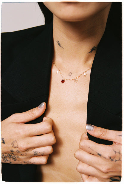 Person wearing a delicate necklace with small pendants, surrounded by tattoos on neck and chest.