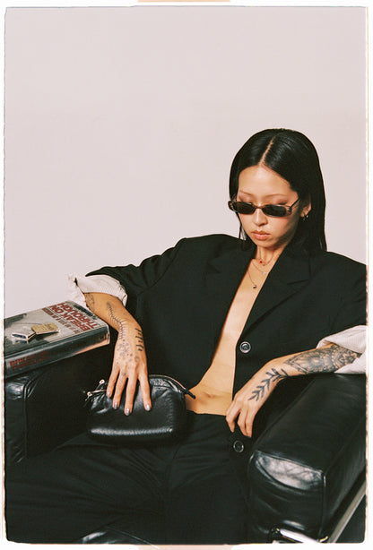 Person wearing a black outfit with sunglasses, sitting on a chair.