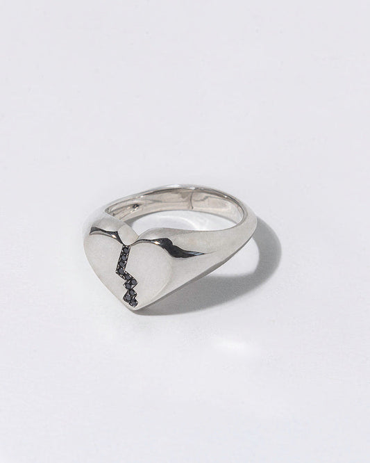 Silver ring with black diamonds in a broken heart shaped signet on a white background