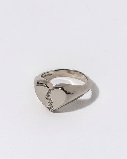 Silver ring with small white diamonds in a broken heart shaped signet on a light gray background