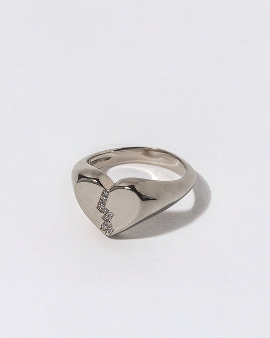 Silver ring with small white diamonds in a broken heart shaped signet on a light gray background