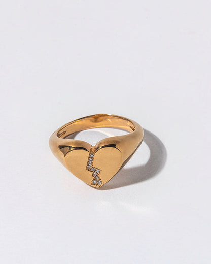 Gold ring with a broken heart-shaped design and embedded white diamonds on a light gray background