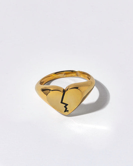 Gold ring with a broken heart design on a light gray background