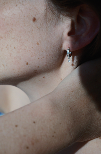 Person wearing a silver hoop with embezzled diamonds and a dangling diamond