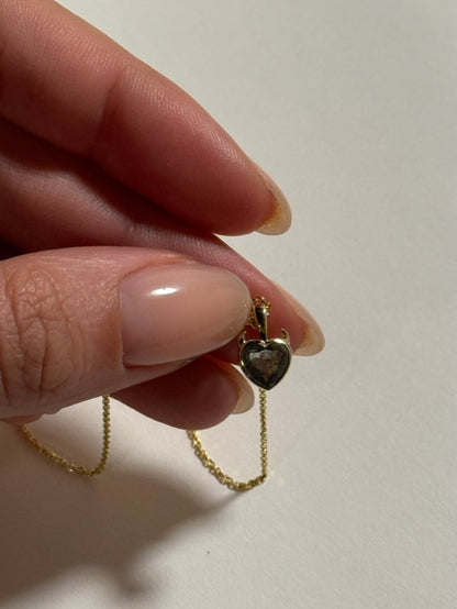 a woman holding a heart shaped diamond pendant with a gold bezel and chain and devil horns 