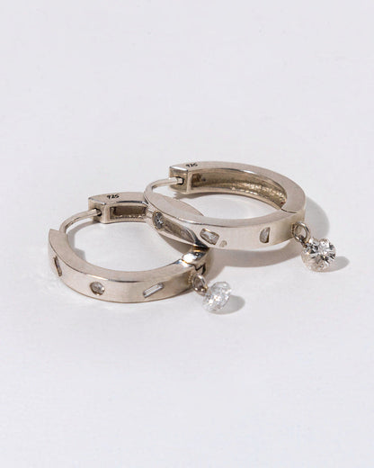 two silver hoops with white diamond bezeled and a dangling diamond on a white background