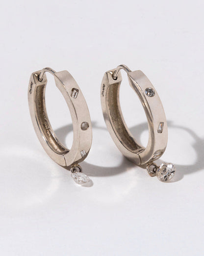 two silver hoops with white diamond bezeled and a dangling diamond on a white background