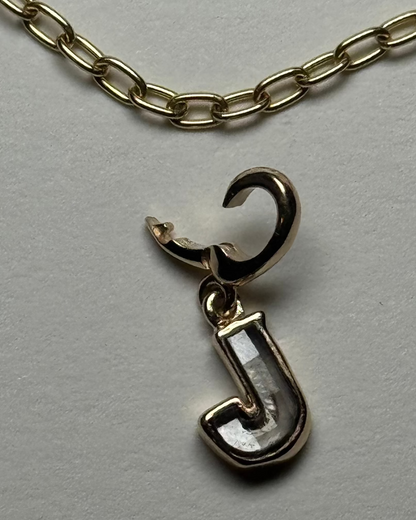 Gold charm with a diamond letter 'J' on a white background and a gold chain