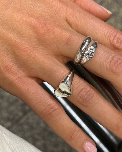 A hand wearing a broken heart sigent ring in silver with black diamonds and two other silver rings 