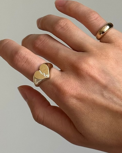 Hand wearing a gold broken heart-shaped ring with white diamonds on a neutral background