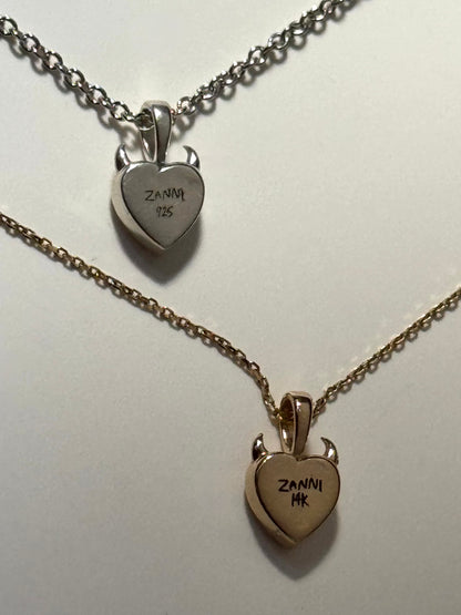 the back of a heart shaped solid silver and gold with devil horns on a chain 
