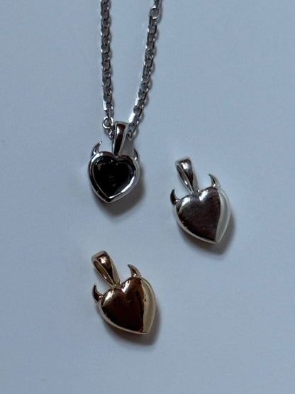 three heart shaped solid gold, and silver pendants with diamonds and devil horns
