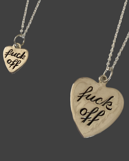 Heart-shaped pendant with 'f**k off' engraving on a chain against a dark background