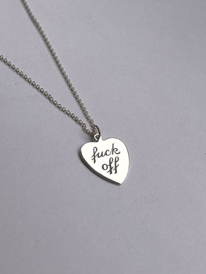 A silver necklace with a small heart-shaped pendant engraved with the phrase 'Fuck Off'.