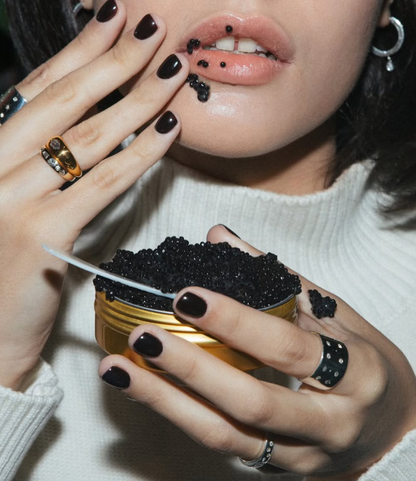 woman eating caviar from a gold tin with black nails and rings on 