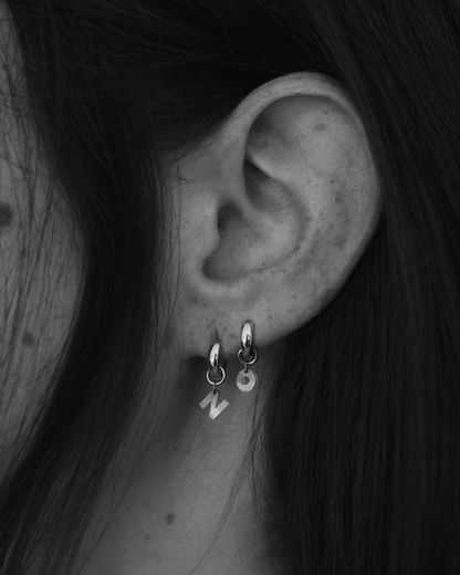 Close-up of an ear wearing two silver hoop earrings with small diamond letter charms.