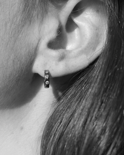 Close-up of an ear wearing a small hoop diamond earring with a blurred background
