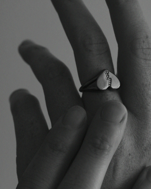 Close-up of a hand wearing a ring with a broken heart design and white diamonds on a plain background