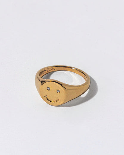 Gold smiley face ring with white diamonds as eyes in a light gray background