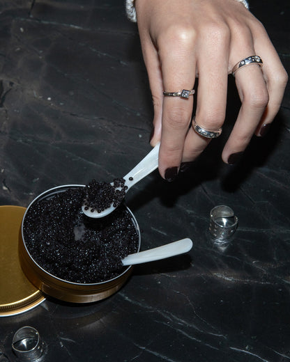 Hand holding a spoon of caviar form a tin while wearing diamond rings