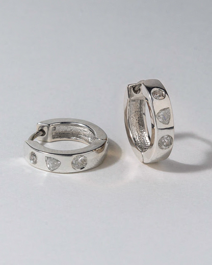 Pair of silver hoop earrings with embedded diamonds on a light gray background