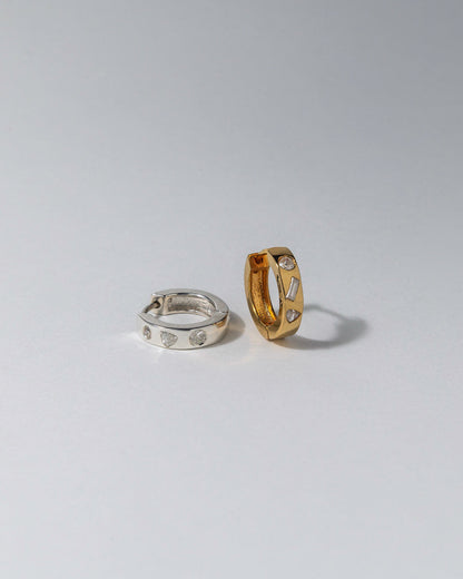 Two diamond hoop earrings, one gold and one silver, on a light gray background
