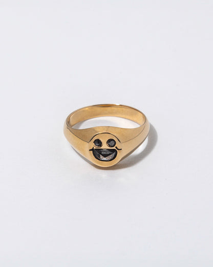 Gold ring with a smiley face design embedded with diamonds on a light gray background