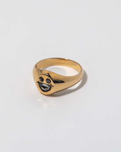 Gold ring with a smiley face design embedded with diamonds on a light gray background