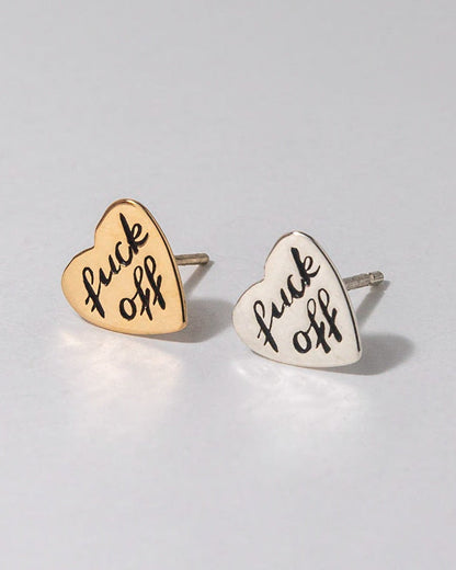 Heart-shaped earrings with 'f**k off' text on a light gray background