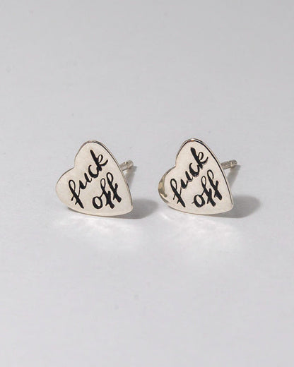 Heart-shaped earrings with 'fuck off' text on a light gray background