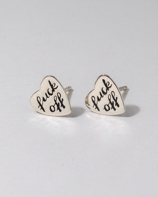 Heart-shaped earrings with 'fuck off' text on a light gray background