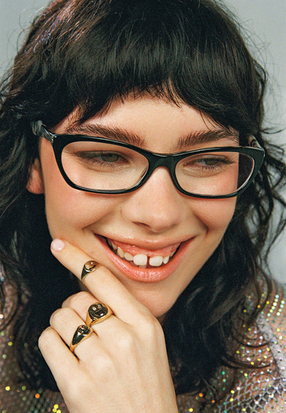 Person wearing black glasses and multiple rings with a sparkly topcoat.