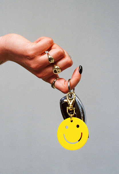 a person holding car keys that has a smiley face key charm and wearing two smiley face gold rings