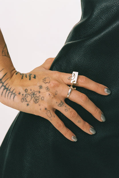 Close-up of a hand with tattoos wearing two rings on a dark green background