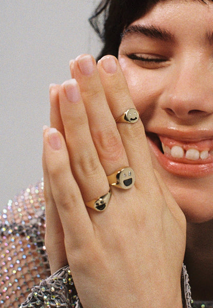 Gold ring with a smiley face design embedded with diamonds on a light gray background