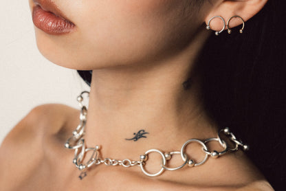 Close-up of a person wearing a silver chain necklace and hoop earrings.