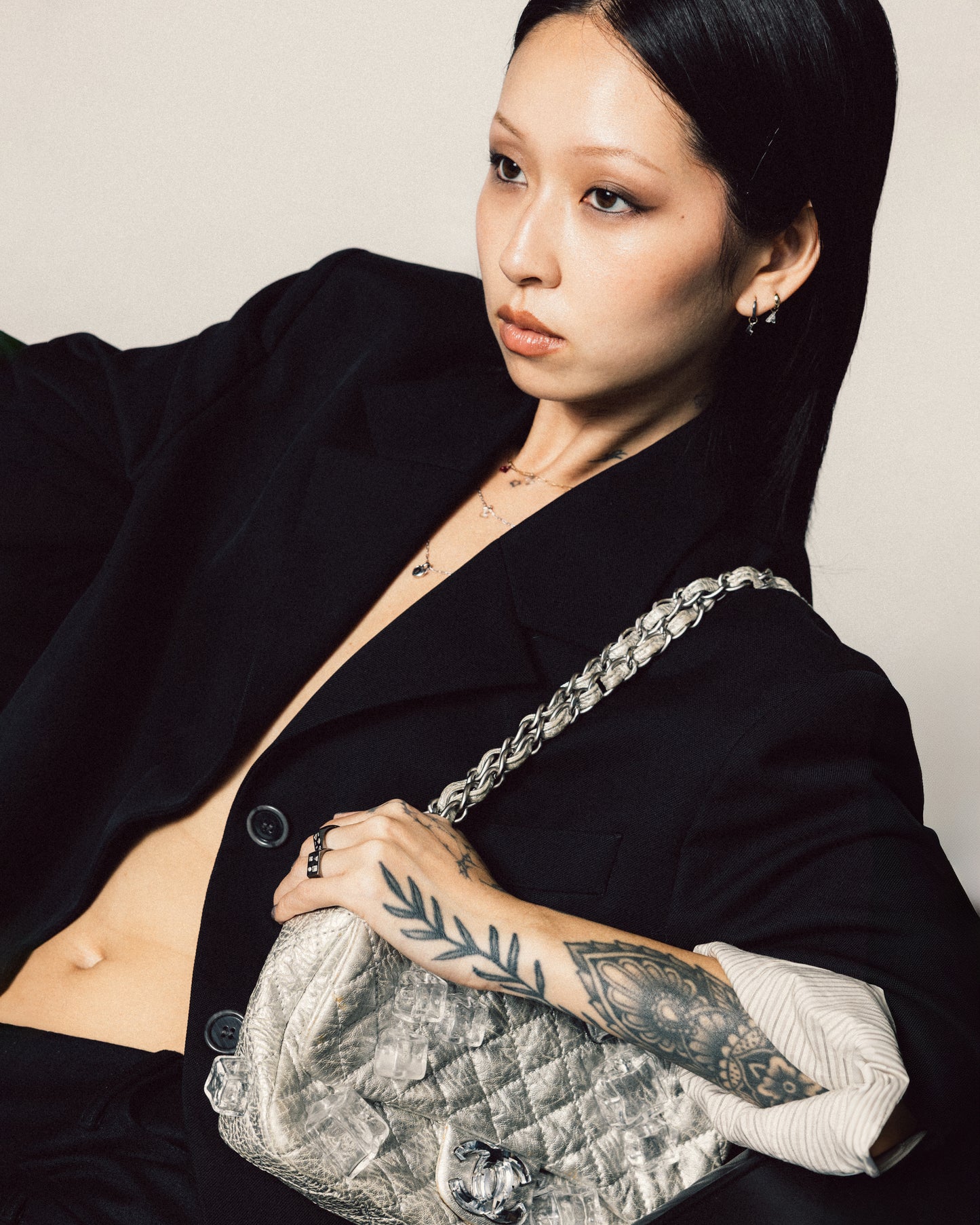 Person wearing a black outfit holding a silver handbag against a neutral background