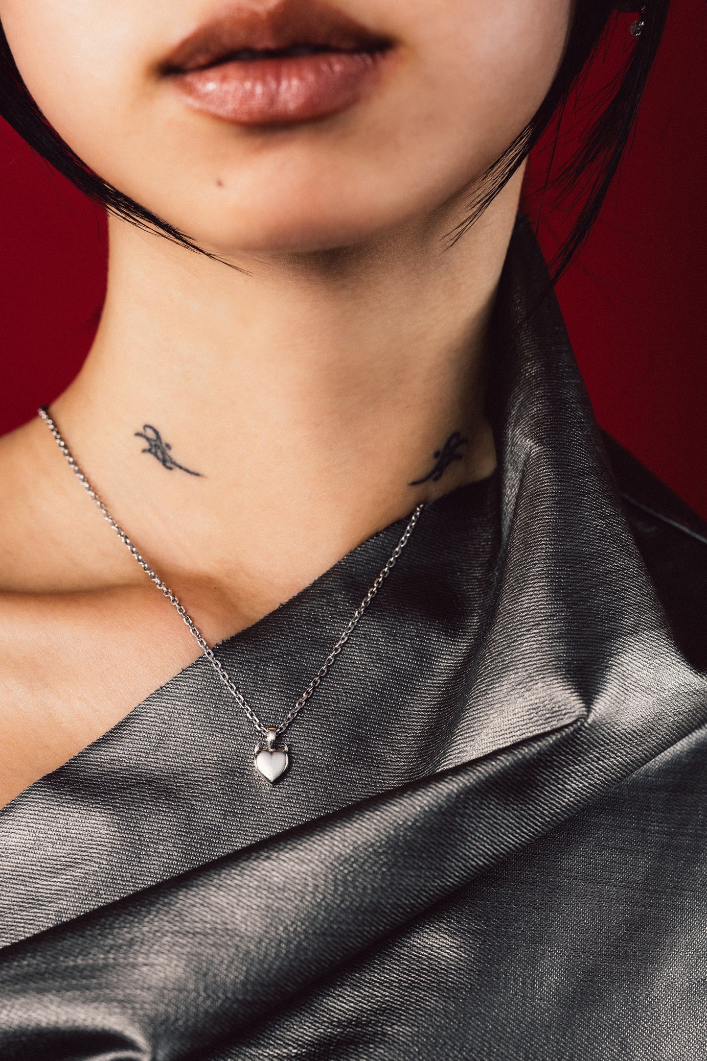 Close-up of a person wearing a silver necklace with a heart pendant against a red background